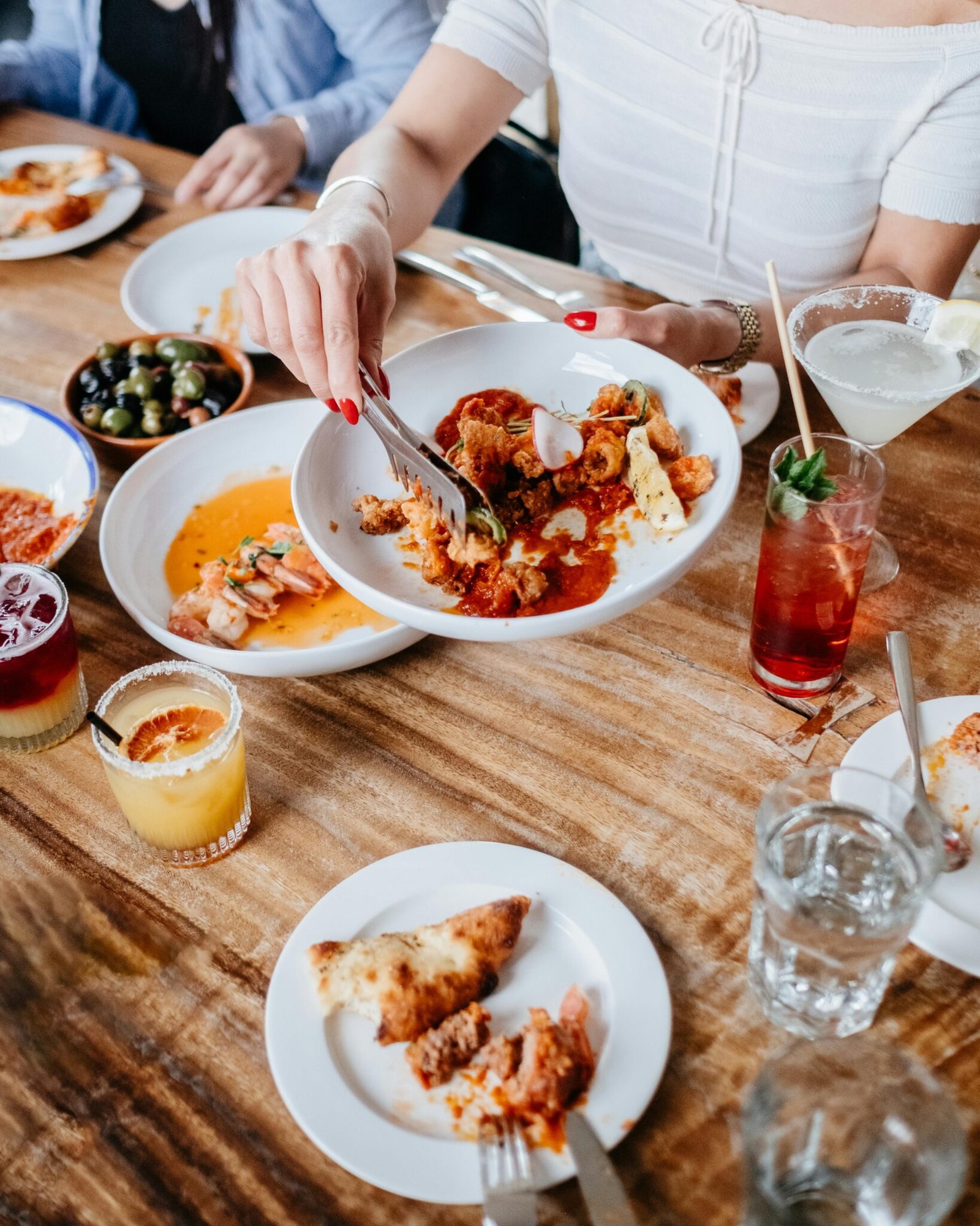 Top view of a dining table with gourmet dishes, drinks, and a woman serving food.